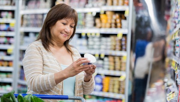 Woman at the grocery store checking for sugar contents on a yogurt label.