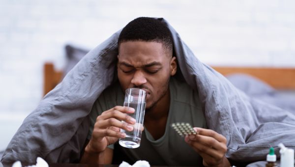 young Black man, sick in bed, drinking a glass of water