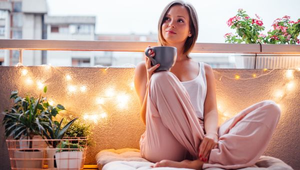 Happy woman surrounded by new home decor enjoying a cup of tea on a balcony.