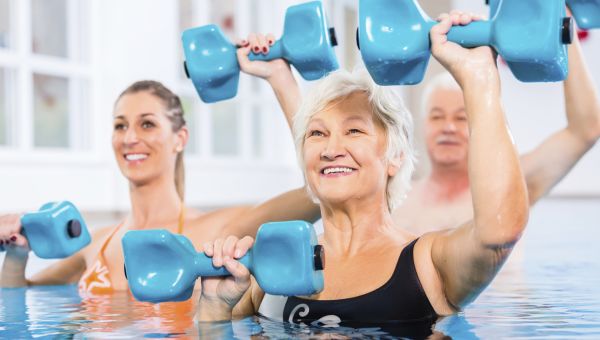 Older person lifting blue dumb bells in a pool group exercise class