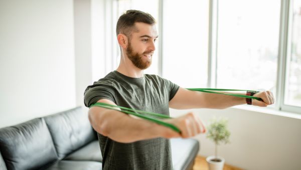 Young man with resistance bands doing an at-home workout in his living room.