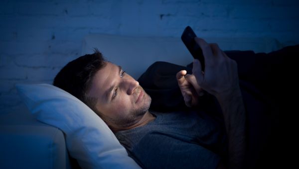 man awake in bed looking at his phone