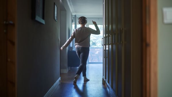 a woman is seen at the end of a hallway in her home happily dancing and listening to music on headphones