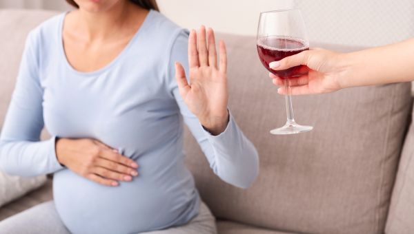 Pregnant person holding up hand as if to say no thank you to someone offering a glass of red wine