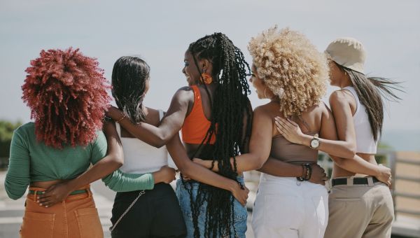 Back view of five people with different hair types and their arms around each other