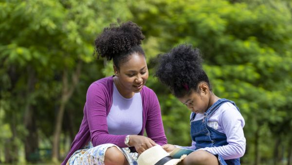 a young Asian American woman reads to her daughter on a beautiful day in a park