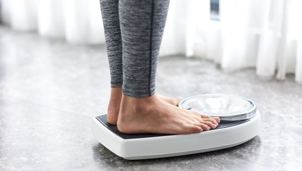 a shot of a white woman's feet and ankles as she stands on a scale to measure her weight