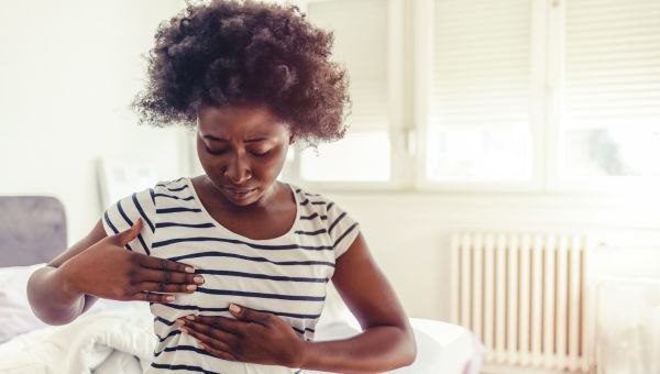 woman in her bedroom sitting on the bed doing a self breast exam