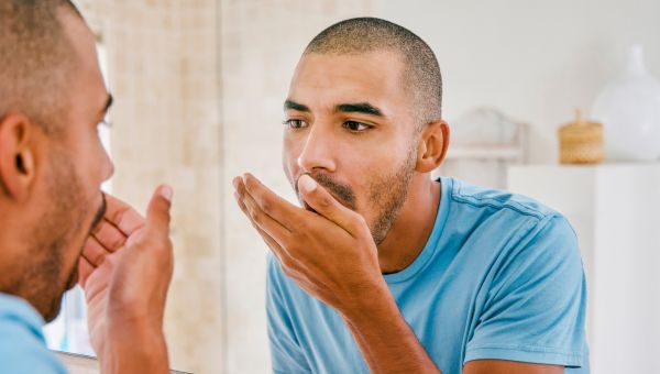 man checking his breath in the bathroom mirror