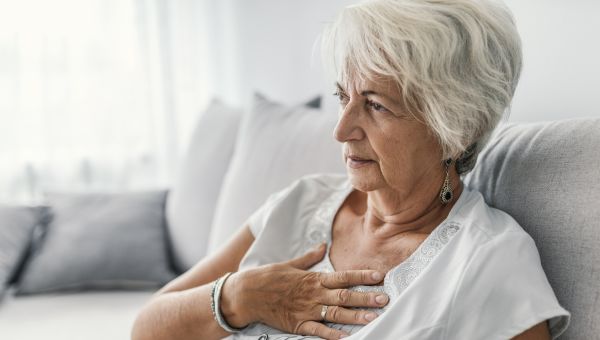 senior woman sitting on her couch holding her chest due to heartburn pain