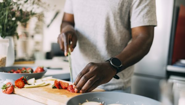 man cutting up strawberries on a cutting board in his kitchen