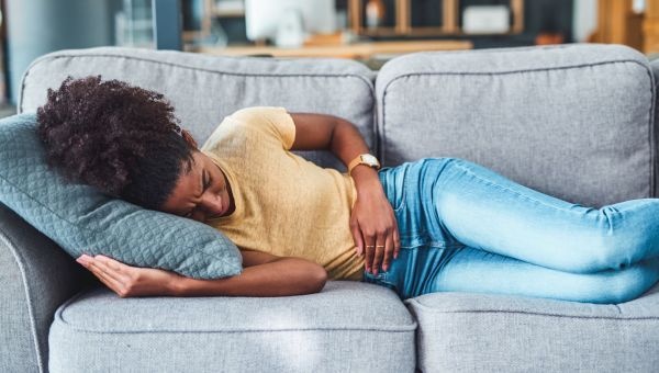 a woman clutching her stomach in period pain on the couch