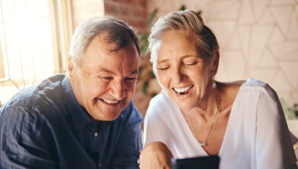 an older couple laughs as they enjoy looking at a cellphone