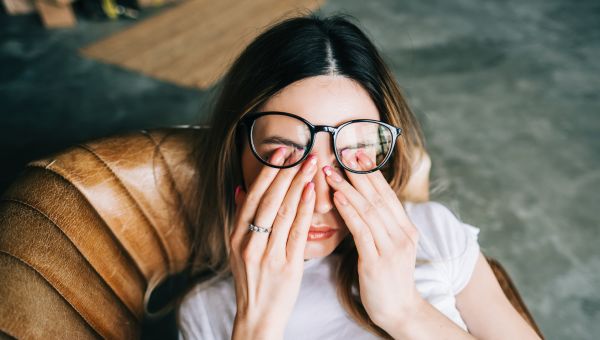 young woman lying back on couch, tired and rubbing her eyes