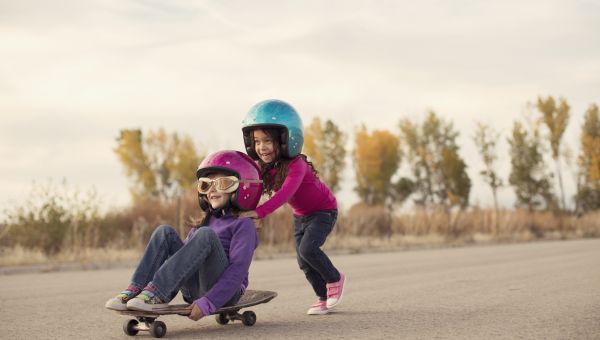 kids wearing helmets riding a skateboard outside