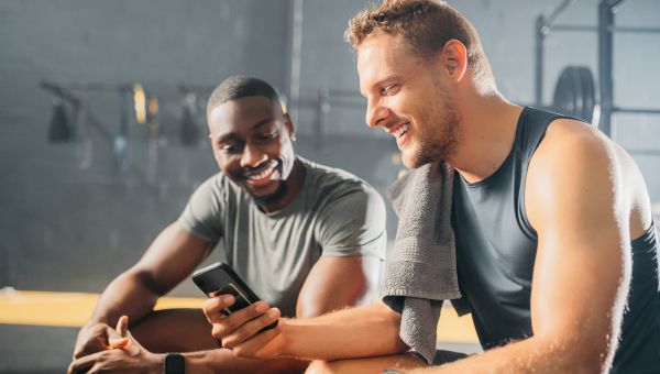 two men at the gym sharing workout ideas looking at a phone together