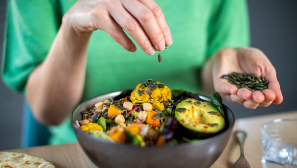 woman sprinkling pumpkin seeds on buddha bowl