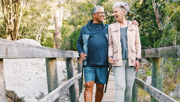 an elderly Latino man and a white woman go for a walk down a nature trail using Nordic poles 