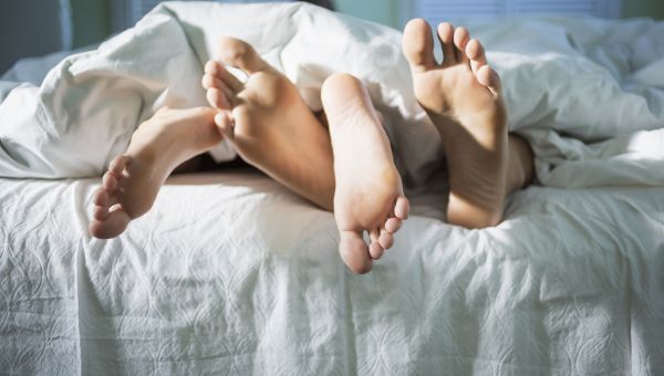 a pair of feet dangles out from underneath a bedsheet, implying a couple having sex