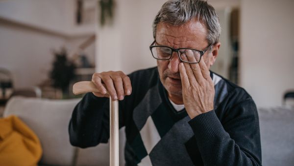 an elderly man rubs his eyes, experiencing vision loss
