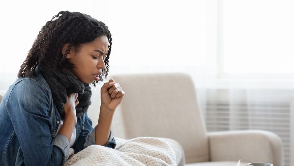 Black woman sitting on bed, sick with a cold or the flu and coughing
