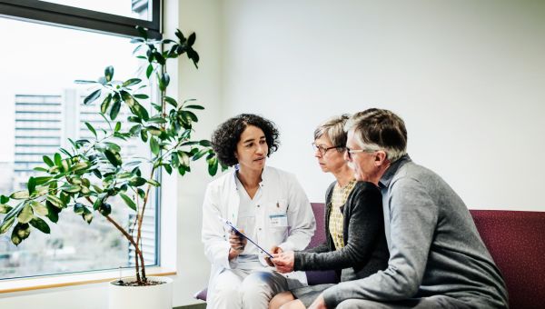 an older adult white man and woman speak with their doctor, a middle aged Middle Eastern woman, about risks of colorectal cancer