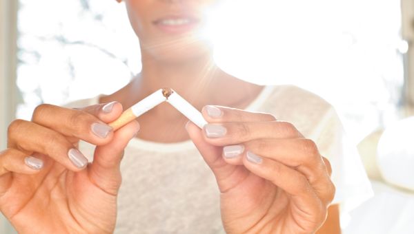 a white woman bathed in bright sunlight breaks a cigarette in half to symbolize her efforts to quit smoking