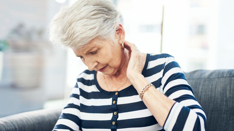 Older woman sitting on a couch with neck pain.