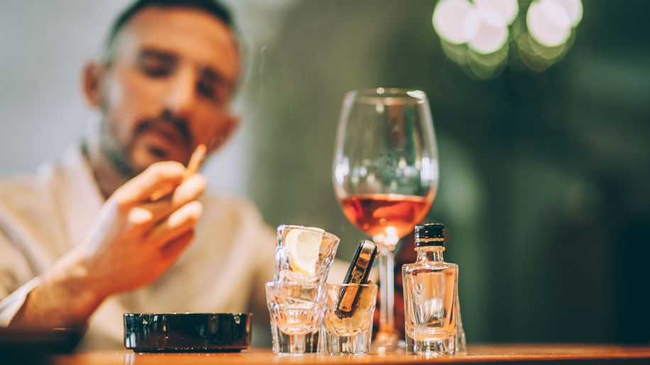 Man smoking a cigarette while drinking heavily.