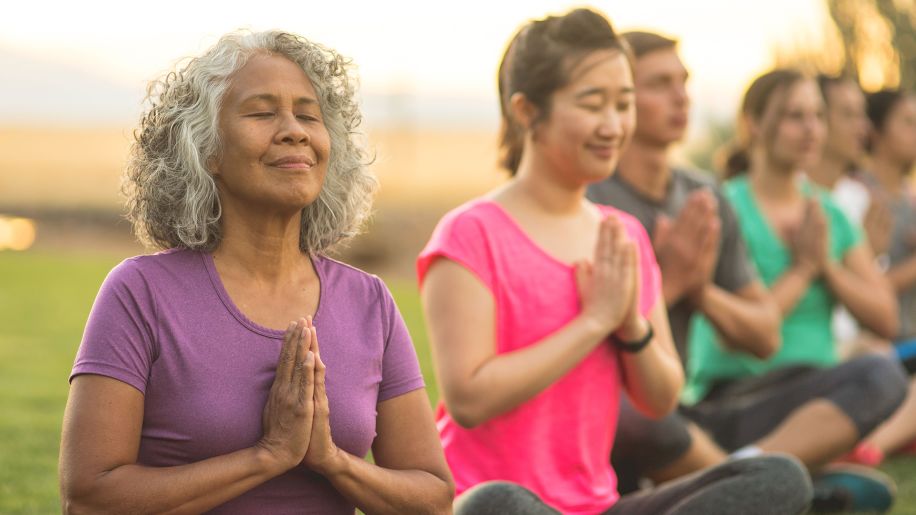 Women's yoga group meditating together outside.