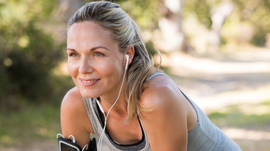 Woman in workout gear taking a rest outside while wearing headphones.