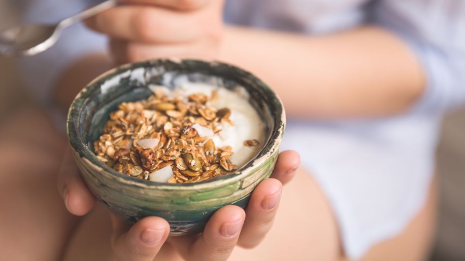 young woman holding a bowl of granola served over yogurt
