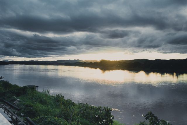 Sun setting over a tranquil river with dark clouds in the sky.