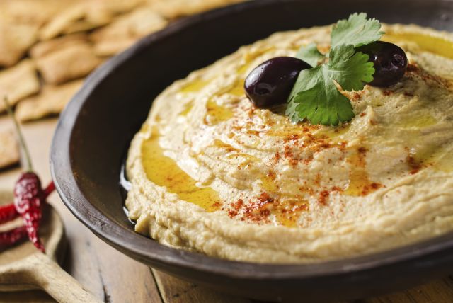 A bowl of creamy chick pea hummus with olive oil and pita chips.