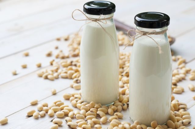 Soy milk in  glass bottle with soy pods on white wooden background, healthy drink