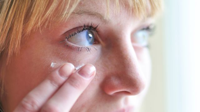 A woman applying cream around her eyes.
