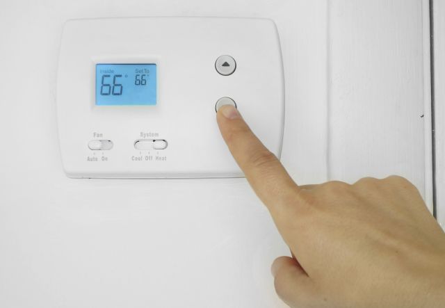 Person's hand adjusting a wall mounted thermostat temperature