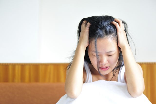 Woman sitting up in bed with her hands in her hair, having a difficult time coping with grief.
