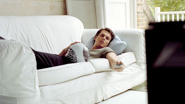 Man lying on sofa using television remote control