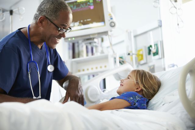 Young girl in a hospital bed talking to a nurse at a local pediatric emergency room.