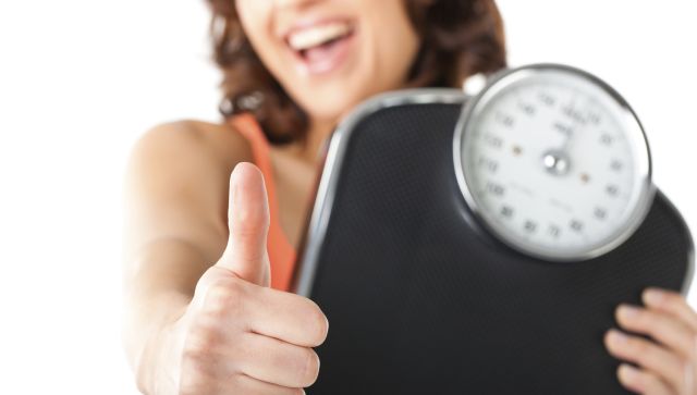 Diet and weight: young woman with a scale; she is happy about the success