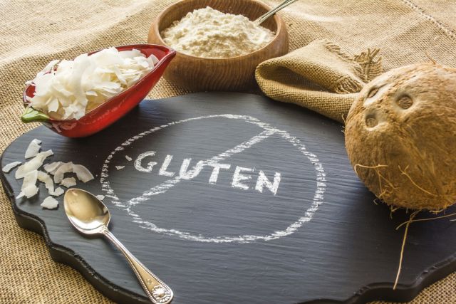 A cutting board with the word "gluten" crossed out, surrounded by coconut and other foods for people going gluten-free.