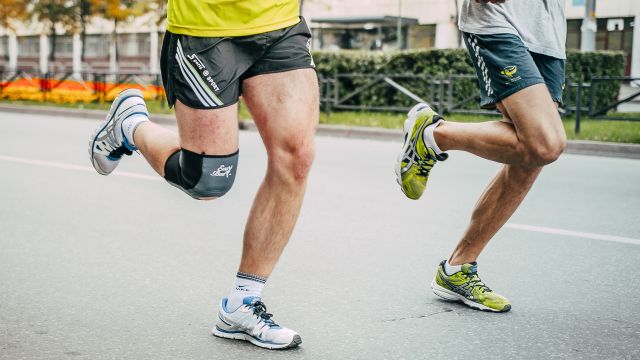 Two runners know how common knee injuries are. One wears a knee brace and often uses RICE therapy for a knee injury.