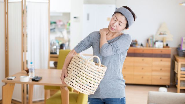 A woman carrying a basket rubs her shoulder in pain. She is in the first of the frozen shoulder stages.