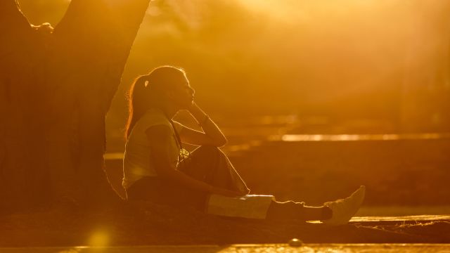 A young woman sitting alone underneath a tree