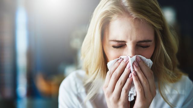 Woman with the flu blowing her nose into a tissue