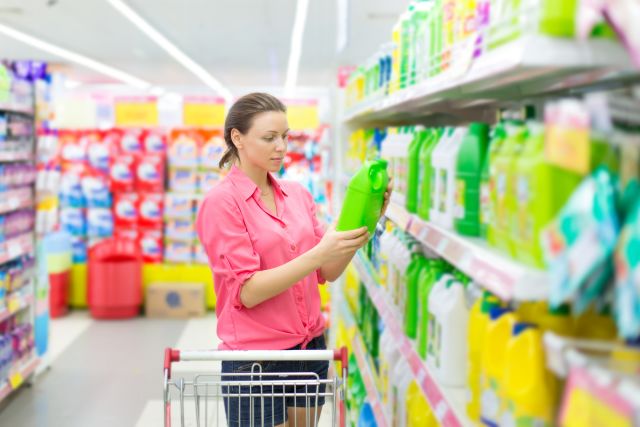 Woman in pink shirt reading label for detergent at grocery store