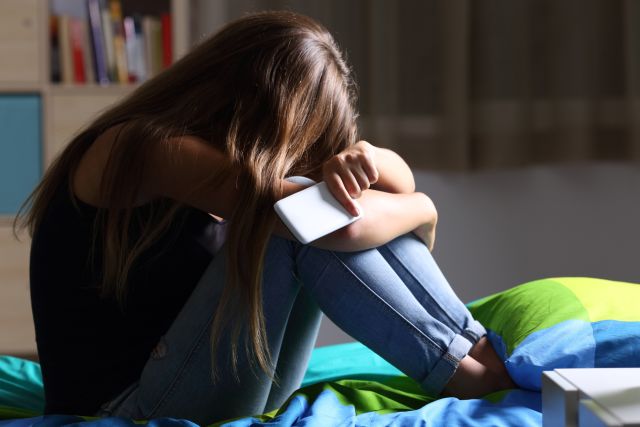 teen girl, head down holding cell phone in her room