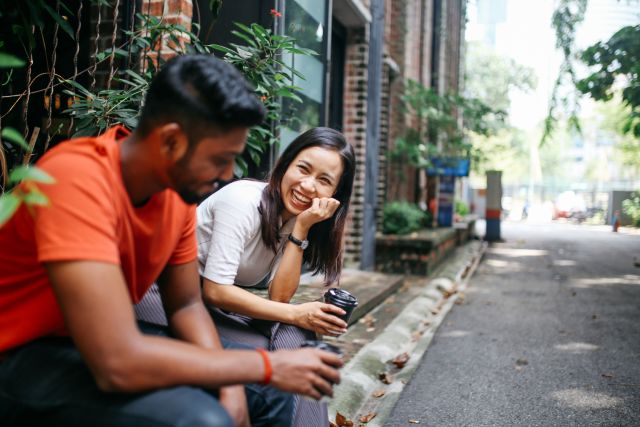 Young Asian man and woman smiling drinking coffee outdoors