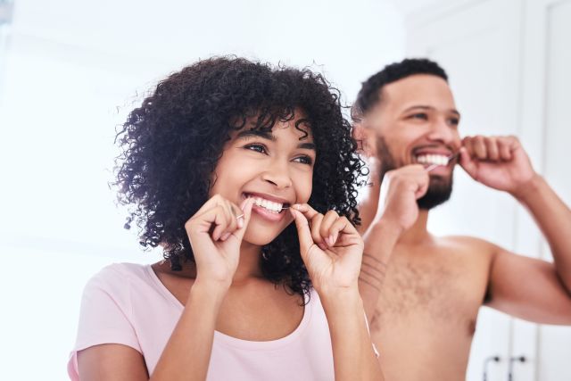 A man and woman brush their teeth to promote oral health—and prevent gum disease and heart disease. 